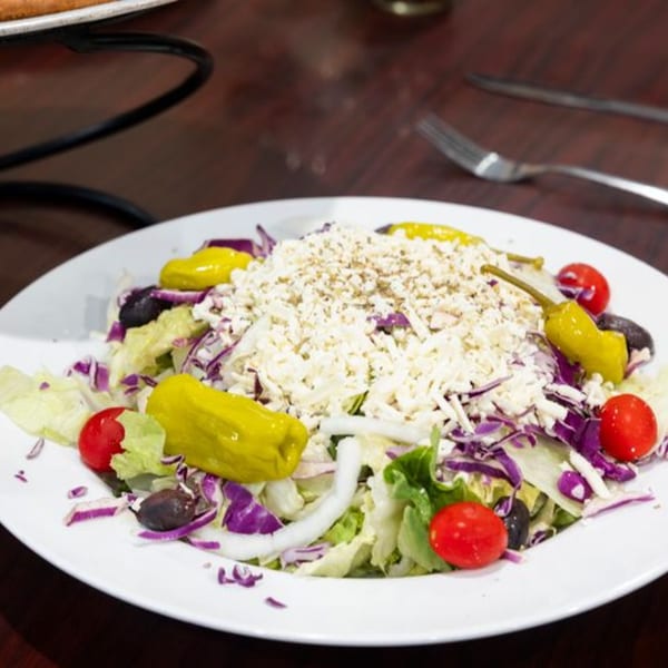 A fresh salad with lettuce, red cabbage, tomatoes, olives, banana peppers, and feta cheese.