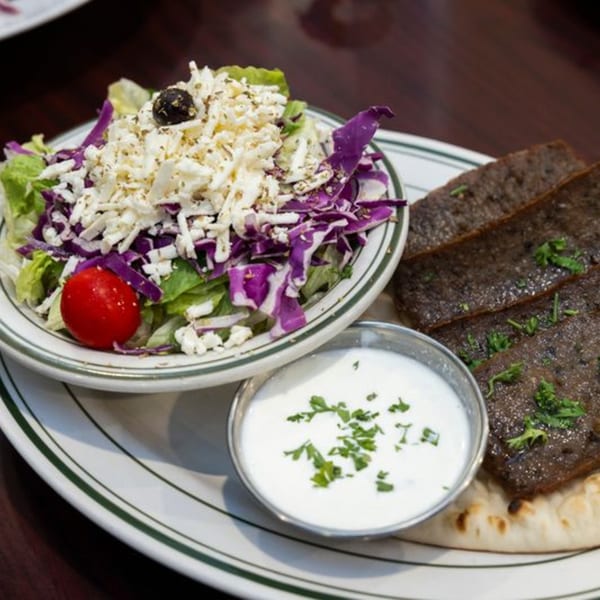 A plate of gyro meat, a side salad with feta and a cherry tomato, and a cup of tzatziki.