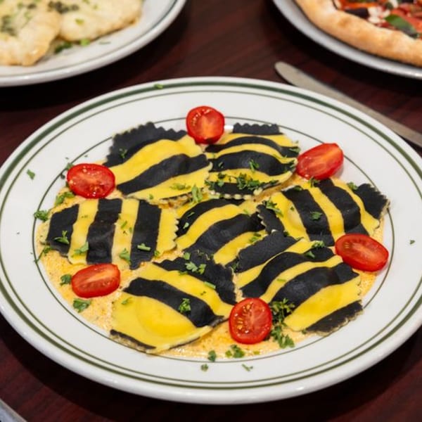 Black and yellow striped ravioli with cherry tomatoes and herbs on a white plate.