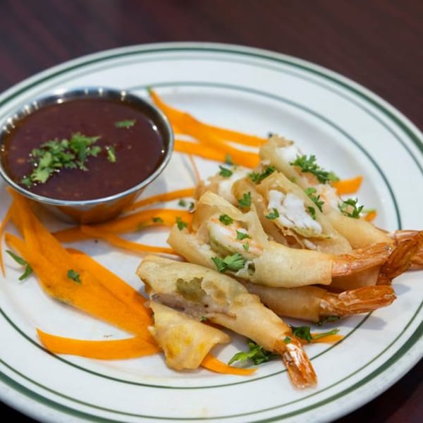 Crispy fried shrimp spring rolls with a side of dark dipping sauce, garnished with parsley and carrot strips.