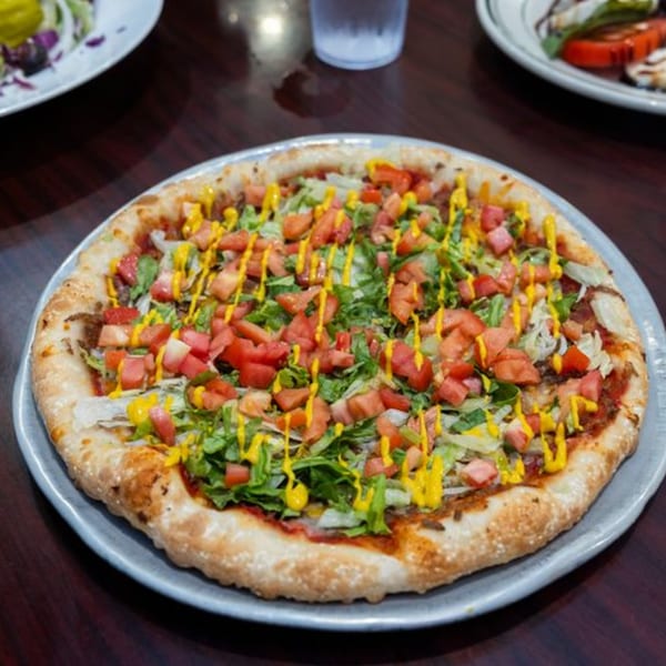 A fully loaded taco pizza with ground beef, lettuce, tomatoes, and a mustard drizzle.