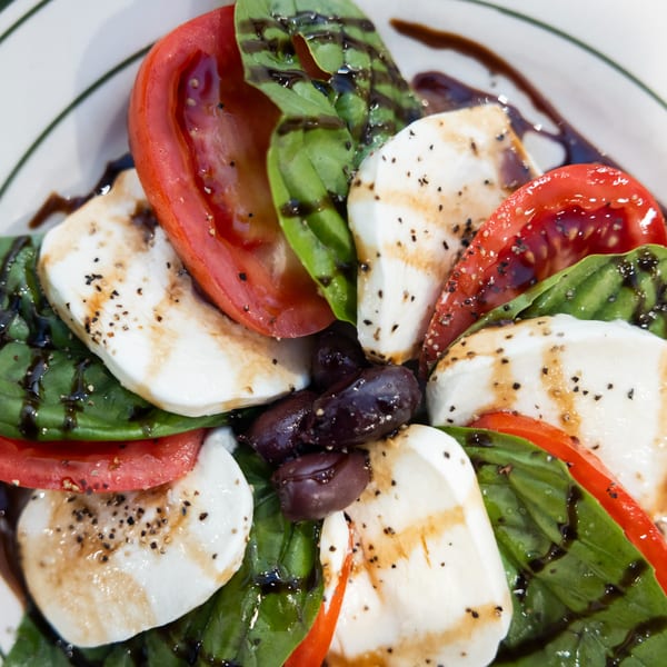 Caprese salad with fresh mozzarella, sliced tomatoes, basil, olives, and balsamic glaze.