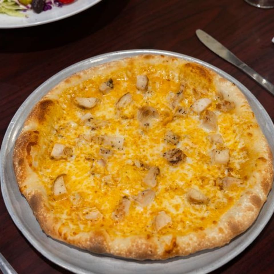 A golden-crusted pizza with melted yellow cheese and chicken pieces on a metal pan.